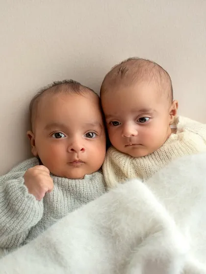 A close-up of the twins snuggled together under a soft white blanket. Capturing their closeness is what twin photography is all about.