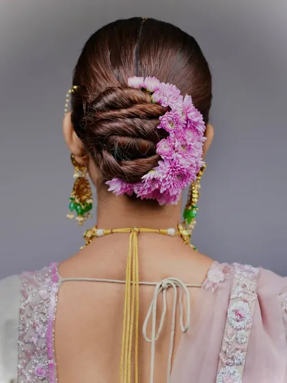 This is the kind of high-end, polished work you'll learn to create. This detailed shot shows a twisted bridal bun, perfectly adorned with a crescent of fresh pink flowers, a style that is both elegant and timeless.