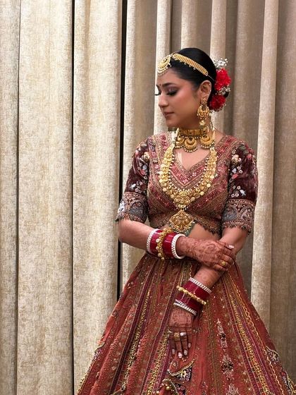 A full view of the traditional bridal look, with a sleek center-parted bun adorned with vibrant red flowers and a matha patti. This is a quintessential bridal hairstyle you will learn to create.