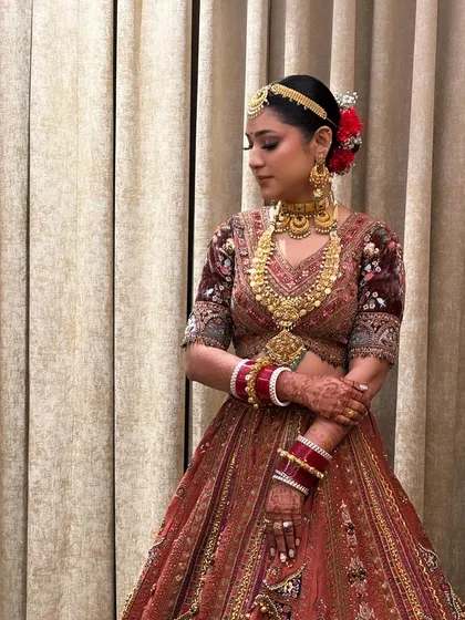 The bride looks serene and beautiful with her classic bridal bun. The red flowers add a pop of color that matches her bangles and the details in her lehenga.