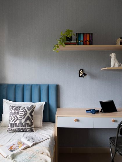 A closer look at the kid's bedroom, focusing on the tranquil grey textured walls, the blue channel-tufted headboard, and the floating study desk.