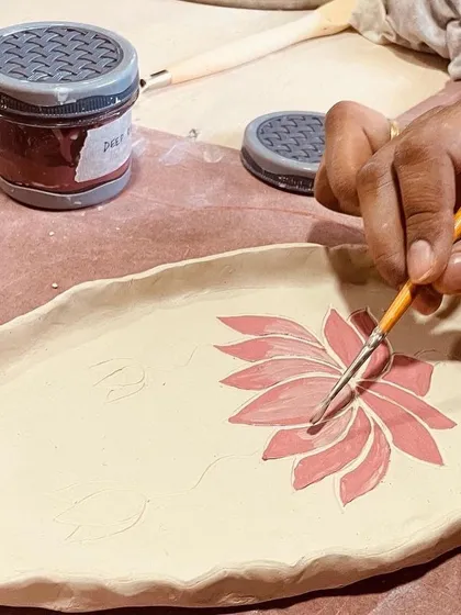 A close-up of a student painting a lotus flower onto a platter. The fine brushwork adds a beautiful, artistic touch.