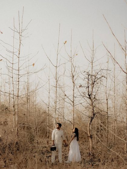 A couple stands together in a rustic, wooded area with bare trees. This earthy and organic setting provides a unique, minimalist backdrop for their pre-wedding portrait.