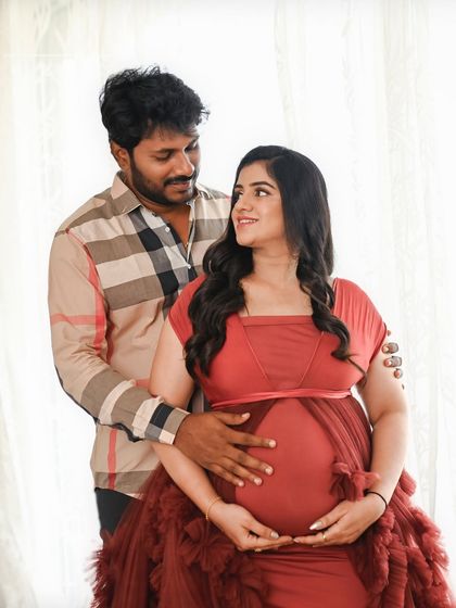 A classic standing portrait against a bright window. The soft light illuminates them, creating a warm and glowing image of the expecting couple.