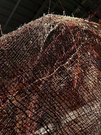 A detail of a large woven sculpture from 'Cu+Fibers'. The image shows the intricate play of hand-spun hemp and shimmering copper wire, creating a rich and complex surface.