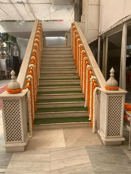 Even stairways become part of the decor. Here, the railings are adorned with alternating garlands of marigold and jasmine flowers, carrying the festive theme throughout the venue.