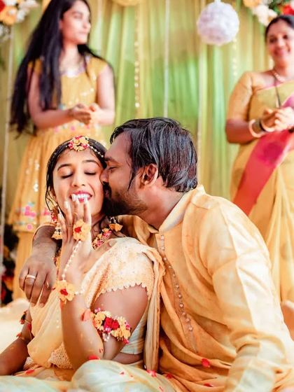 A sweet and intimate moment, with the groom giving the bride a kiss on the cheek during their Haldi ceremony.