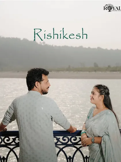 A quiet moment between a couple dressed in elegant ethnic wear, looking at each other on a balcony overlooking the Ganga.