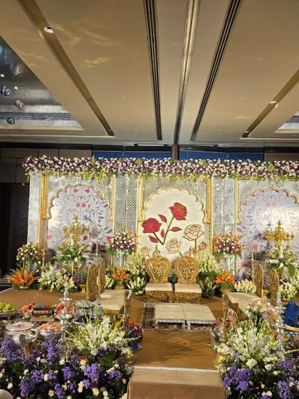 An elegant stage with a painted floral backdrop featuring large roses. The decor is complemented by fresh flower arrangements and ornate gold chairs for the couple.