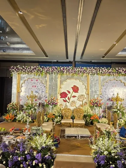 An elegant stage with a painted floral backdrop featuring large roses. The decor is complemented by fresh flower arrangements and ornate gold chairs for the couple.