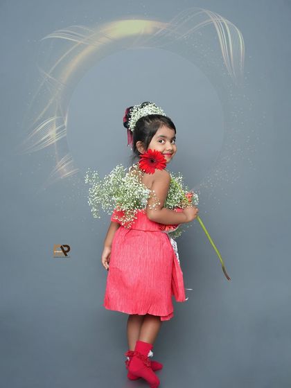 A girl in a flower dress looks back with a smile, holding a single gerbera. This portrait showcases the creativity and artistry of a custom-themed shoot.