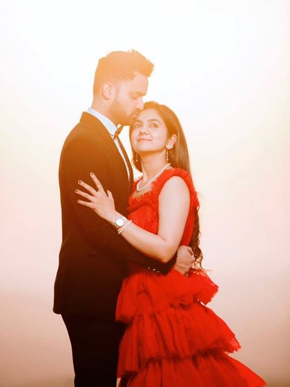 A studio-style portrait with a warm, glowing background. The bride's vibrant red dress stands out beautifully in this romantic and polished pre-wedding photograph.