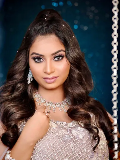 A direct, confident portrait showing the bold eye makeup and the sparkling diamond necklace.