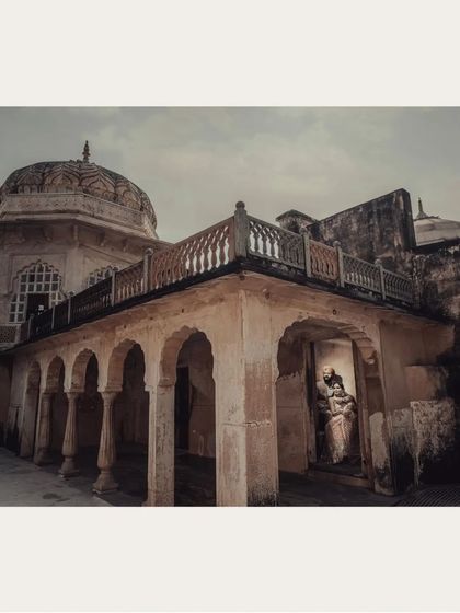 A wide architectural shot that frames the couple in an embrace on a palace balcony. This emphasizes the scale and grandeur of the location.