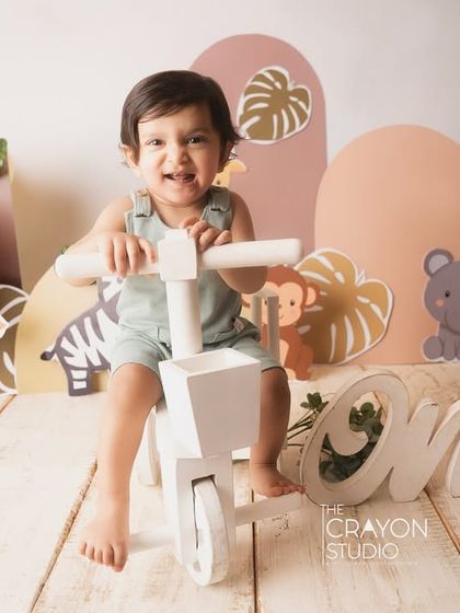 A happy boy on his tricycle, enjoying his jungle-themed first birthday party in the studio.