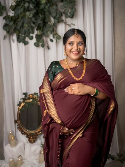 The expectant mother's smile lights up the frame. This portrait captures her happiness and confidence, beautifully styled in a traditional maroon saree and gold jewelry.