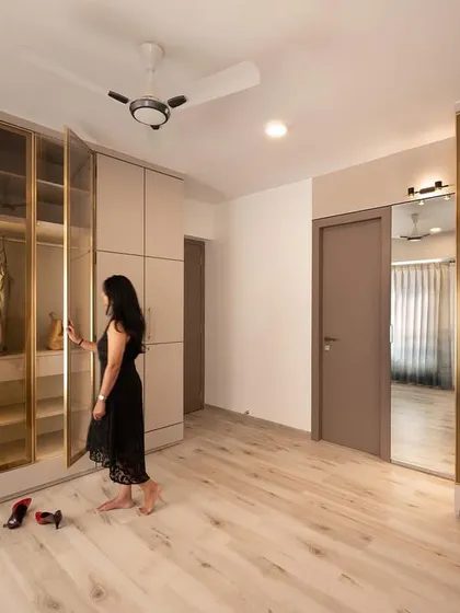 This spacious master bedroom features custom wardrobes with bronze-tinted glass profile shutters. The design provides a mix of open and closed storage, with internal lighting to showcase the contents.