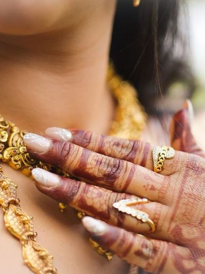 A close-up shot focusing on the details of the jewelry and the henna-stained fingers.