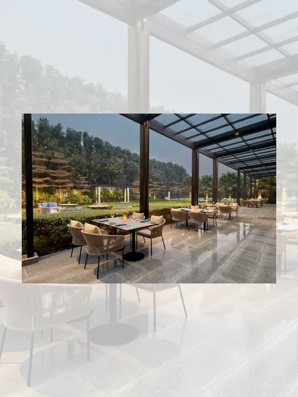 The outdoor dining terrace at the Courtyard by Marriott. The space is covered by a modern pergola with a glass roof, allowing for alfresco dining with views of the hotel's green lawns.