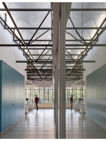 The interior of 'Hoverspace' is a column-free environment where structural trusses are celebrated as sculptural red elements. Minimalist furniture and extensive use of glass for partitions create a transparent, light-filled, and collaborative workspace.