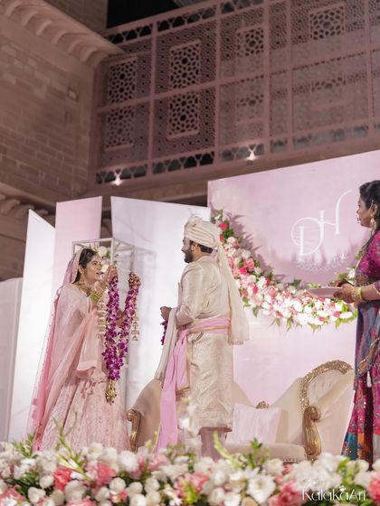 The bride places the varmala on the groom, a key moment in the Hindu wedding ceremony. We capture this from a distance to show the beautiful stage decor and the context of the ritual.