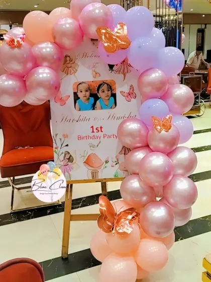 A personalized welcome sign for a twins' first birthday party, adorned with pink balloons.
