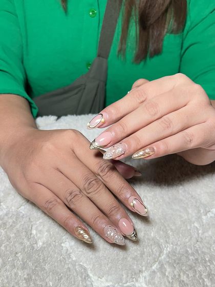 A glamorous set of almond-shaped extensions with a nude base, gold chrome tips, and textured gold accents.