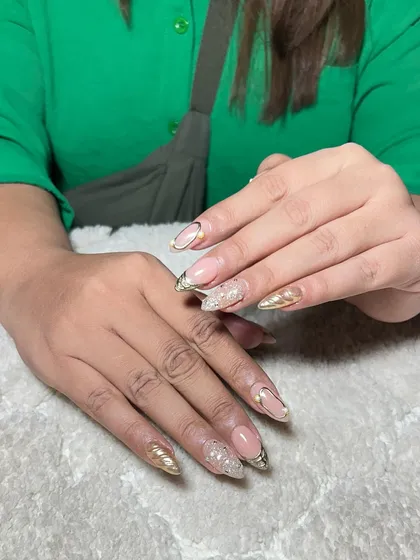 A glamorous set of almond-shaped extensions with a nude base, gold chrome tips, and textured gold accents.