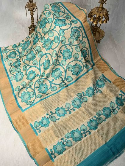The elegance of the lotus flower is captured in this hand-painted Pen Kalamkari saree. The serene blue lotuses are painted on a natural beige tussar silk base, creating a tranquil and artistic effect.