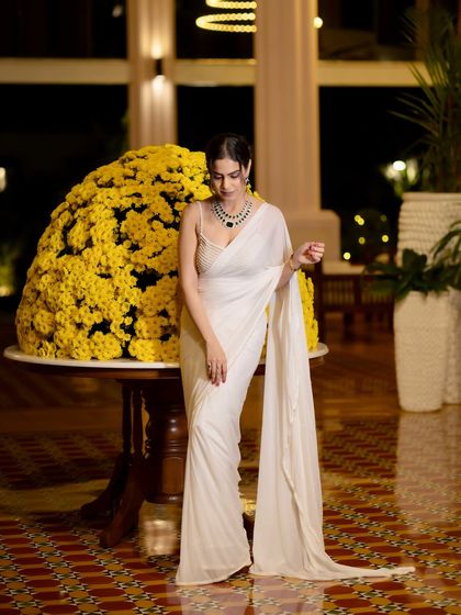 A full-length shot of the white saree against a stunning floral arrangement, showcasing the hotel's beautiful decor.