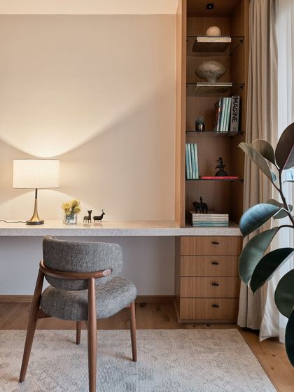 The study nook within the NG Penthouse continues the theme of clean lines and warm materials. A floating stone desk is paired with built-in wooden shelving, creating a functional workspace that feels integrated and uncluttered.