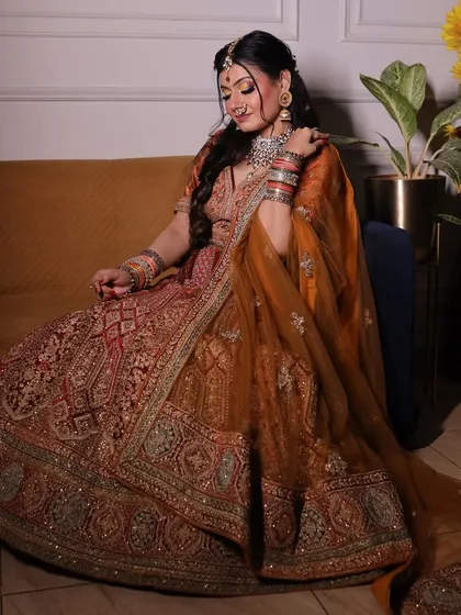 This is the quintessential bridal look. A heavily embroidered lehenga in a rich rust and orange tone, paired with traditional jewelry, captures the timeless elegance every bride dreams of for her wedding day.