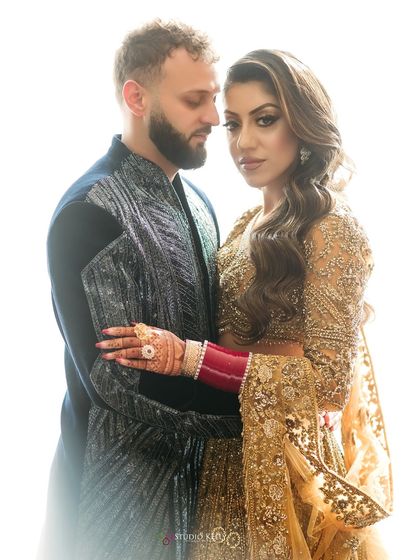 A beautifully lit portrait of the couple from their London reception, highlighting the bride's golden lehenga and traditional red 'chooda' bangles.