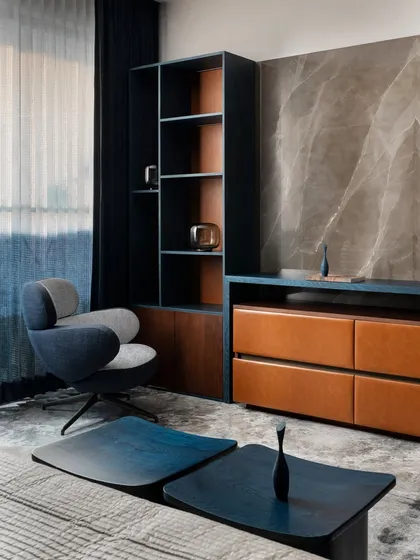 This corner of the master bedroom showcases our focus on custom furniture and material synergy. The blue and grey armchair, bespoke shelving, and leather-fronted drawers create a functional and stylish nook for reading or relaxing.