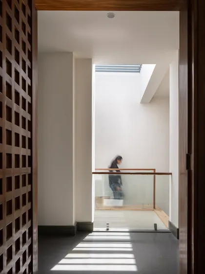 A person stands in the light-filled stairwell, illustrating the verticality of the space. The glass railing and open design ensure that light penetrates deep into the home's core.