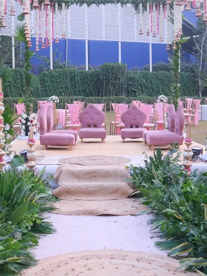 A view of the mandap aisle, lined with lush green foliage and jute mats. This natural pathway leads to the raised stage, creating a beautiful journey for the couple's entrance.