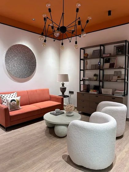 Another view of my studio's lounge area, designed for informal meetings and brainstorming. The combination of the warm orange sofa, textured white chairs, and industrial-style shelving creates a balanced and eclectic workspace.