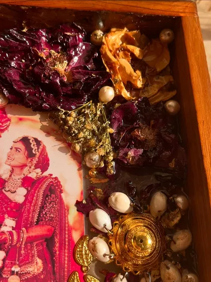 A close-up view of a teakwood frame, highlighting the preserved kaleera, varmala flowers, and other small ornaments. Each element is carefully placed to create a balanced and beautiful composition.