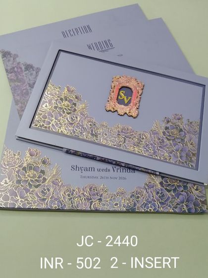 This lavender invitation features a framed design with intricate gold and purple floral laser-cutting. A custom 'SV' monogram adds a personal touch to this elegant, two-insert card.