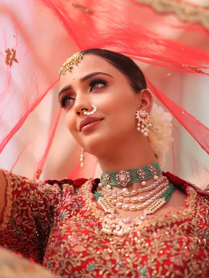 Peeking through the veil. I love styling with a sheer red dupatta to create a sense of romance and anticipation, perfectly framing the bride's intricate jewelry and radiant makeup.