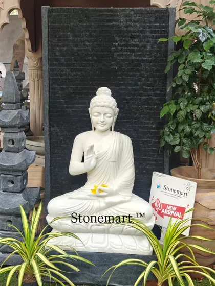 A frontal view of the 5-foot Blessing Buddha fountain, highlighting the contrast between the pure white marble statue and the textured black granite backdrop. The water flows gently over the granite, creating a calming sound.