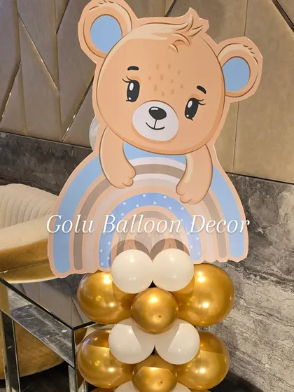 A cute teddy bear and rainbow cutout on a gold and white balloon pillar, perfect for a baby's party.