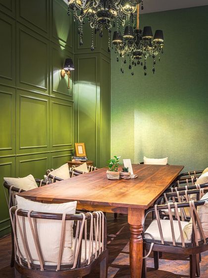 This private dining area at EVE Bombay features rich green paneled walls and a dramatic black chandelier. The combination of classic wooden furniture and bold color creates a sophisticated and intimate setting for memorable gatherings.