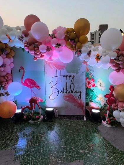 A beautiful flamingo-themed birthday on a rooftop, with a tropical print backdrop, flamingo props, and a pink and white balloon arch.