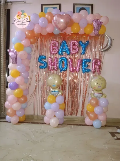 A pastel-colored baby shower decoration with a balloon arch, shimmer curtain, and baby-themed foil balloons.