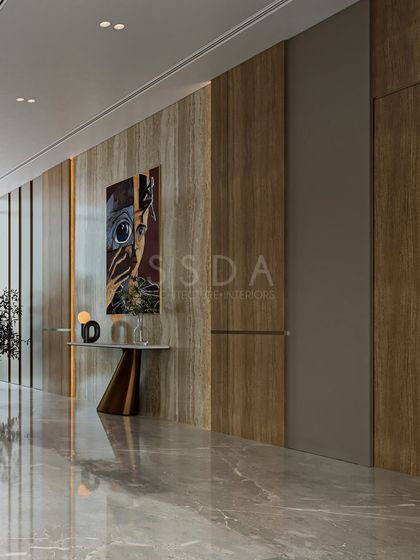 A detail of a common area in an upcoming villa, where a wood-veneered wall and a modern console table are punctuated by a bold piece of art. The polished marble floor reflects the light beautifully.