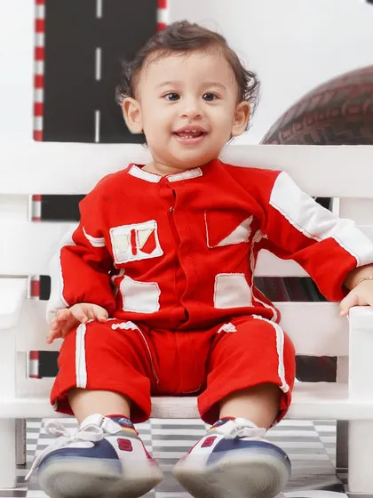 Ready, set, go! A cute baby boy in a red racing suit smiles for the camera in a fun, race-car themed photoshoot.