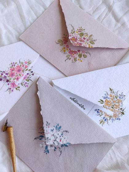 A stunning array of the hand-painted envelopes, showcasing different color schemes and floral arrangements. Each one is a unique piece of art.