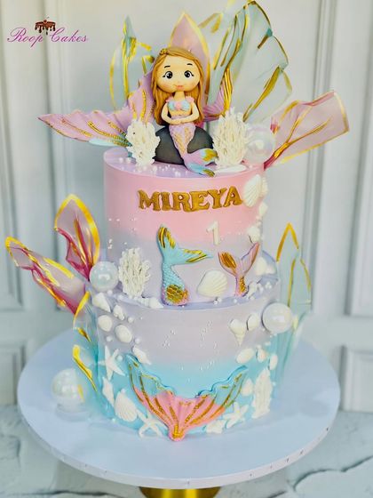 A stunning two-tier mermaid cake with an iridescent theme. The design features a beautiful fondant mermaid, shimmering rice paper sails, and under-the-sea details in pastel colors.