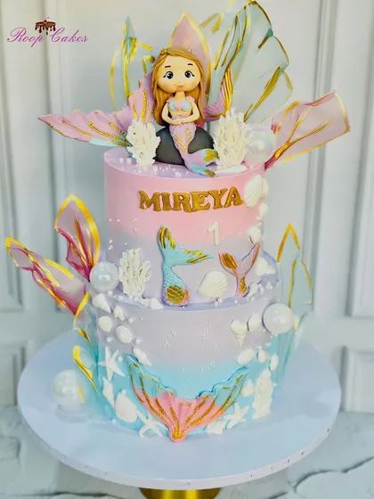 A magical two-tier mermaid theme cake with iridescent fins, seashells, and a beautiful fondant mermaid.
